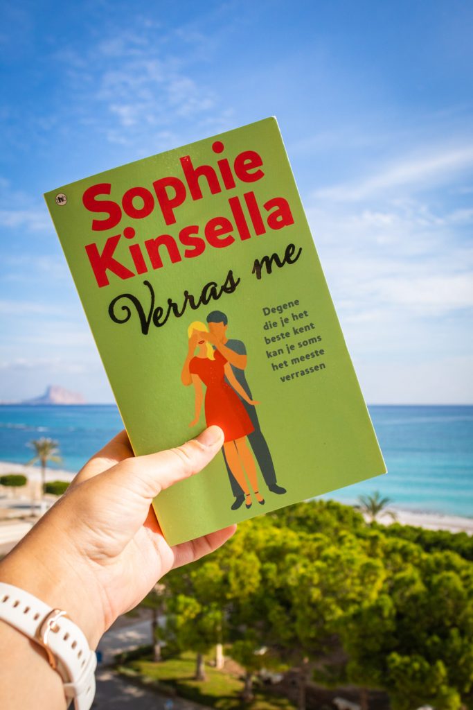 Het boek Verras Me van Sophie Kinsella omhoog gehouden voor de zee