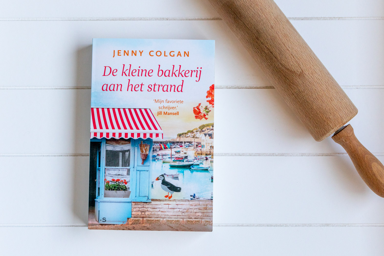 Het boek De kleine bakkerij aan het strand van Jenny Colgan met een deegroller ernaast