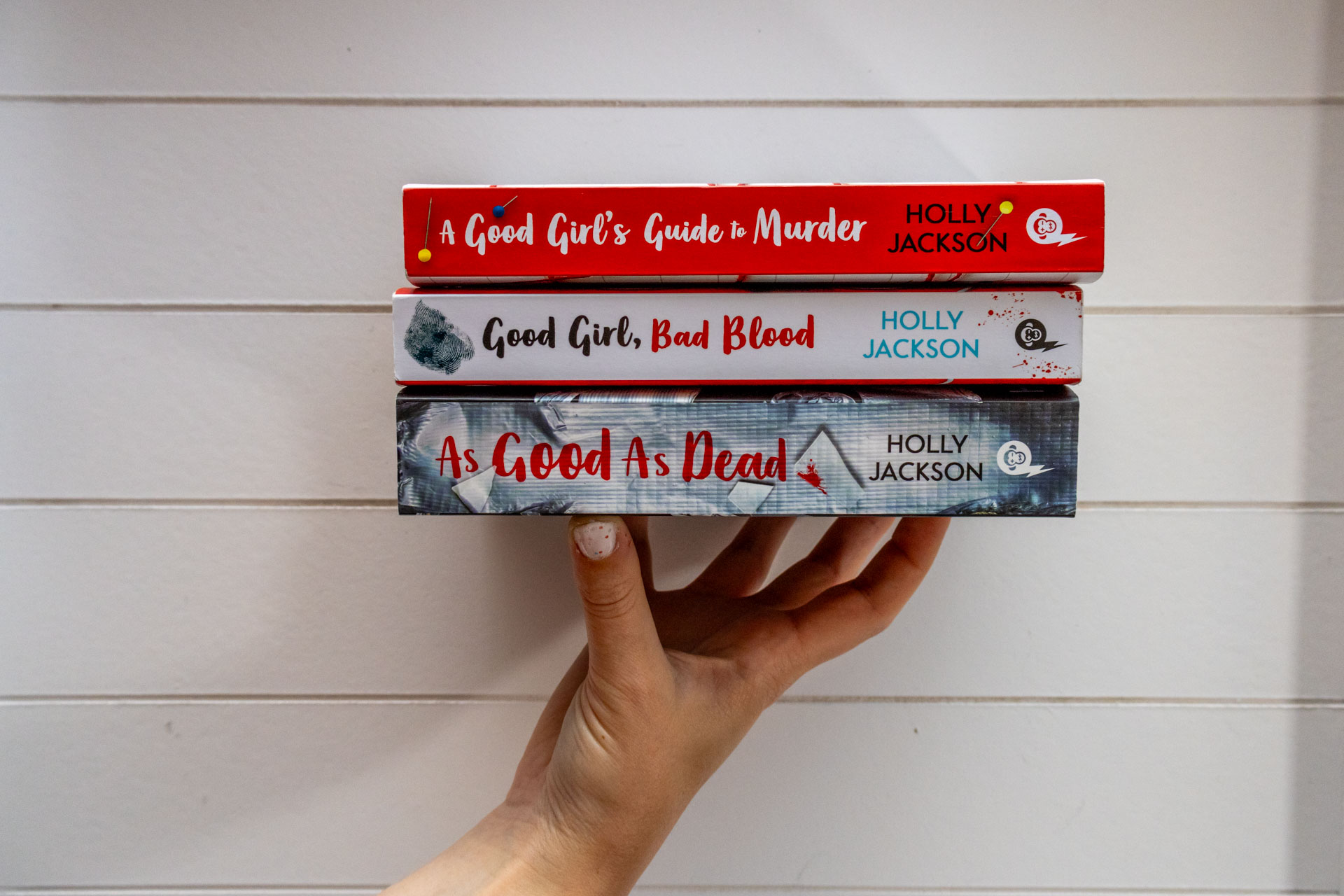 De serie van Holly Jackson, A Good Girl's Guide to Murder, op een stapeltje op de hand van Manouk op een witte achtergrond