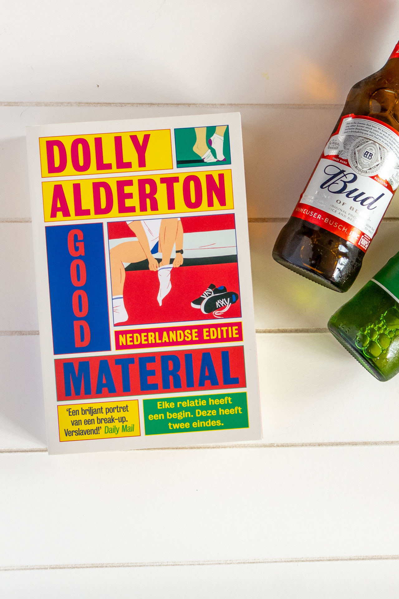 Nederlandse editie van het boek Good Material van Dolly Alderton in paperback met enkele biertjes ernaast