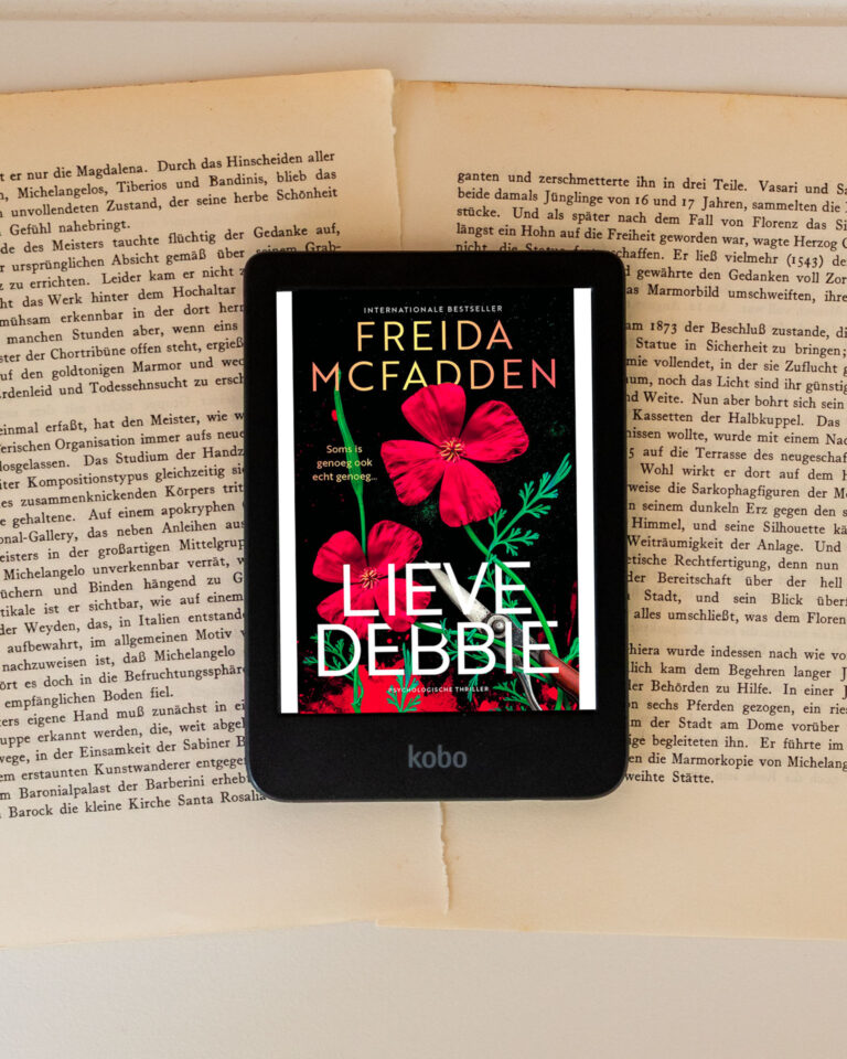 Het e-book Lieve Debbie van Freida McFadden wordt weergegeven op een e-reader die op opengeslagen boekpagina’s ligt. Op het scherm is de zwarte cover te zien met rode bloemen, groene stelen en de titel Lieve Debbie in grote witte letters, met daarboven de naam van de auteur. Onderaan de e-reader is het Kobo-logo zichtbaar.