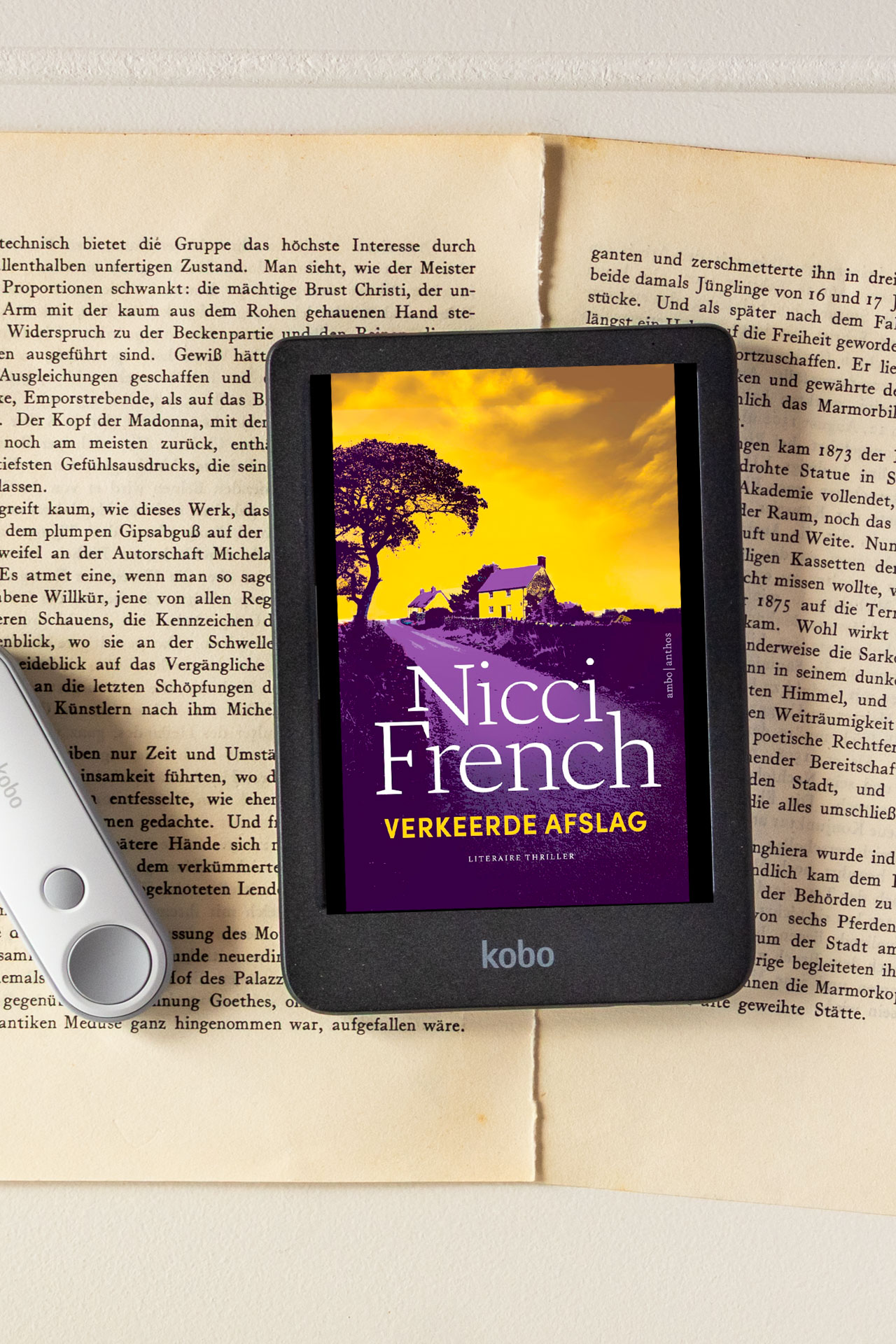 De e-reader toont het e-book Verkeerde afslag van Nicci French en ligt op open, vergeelde boekpagina’s. Op de cover zie je een huis en boom tegen een felgele lucht met paarse tinten, met de titel en auteursnaam duidelijk leesbaar. Links naast de e-reader ligt een witte afstandsbediening deels in beeld.