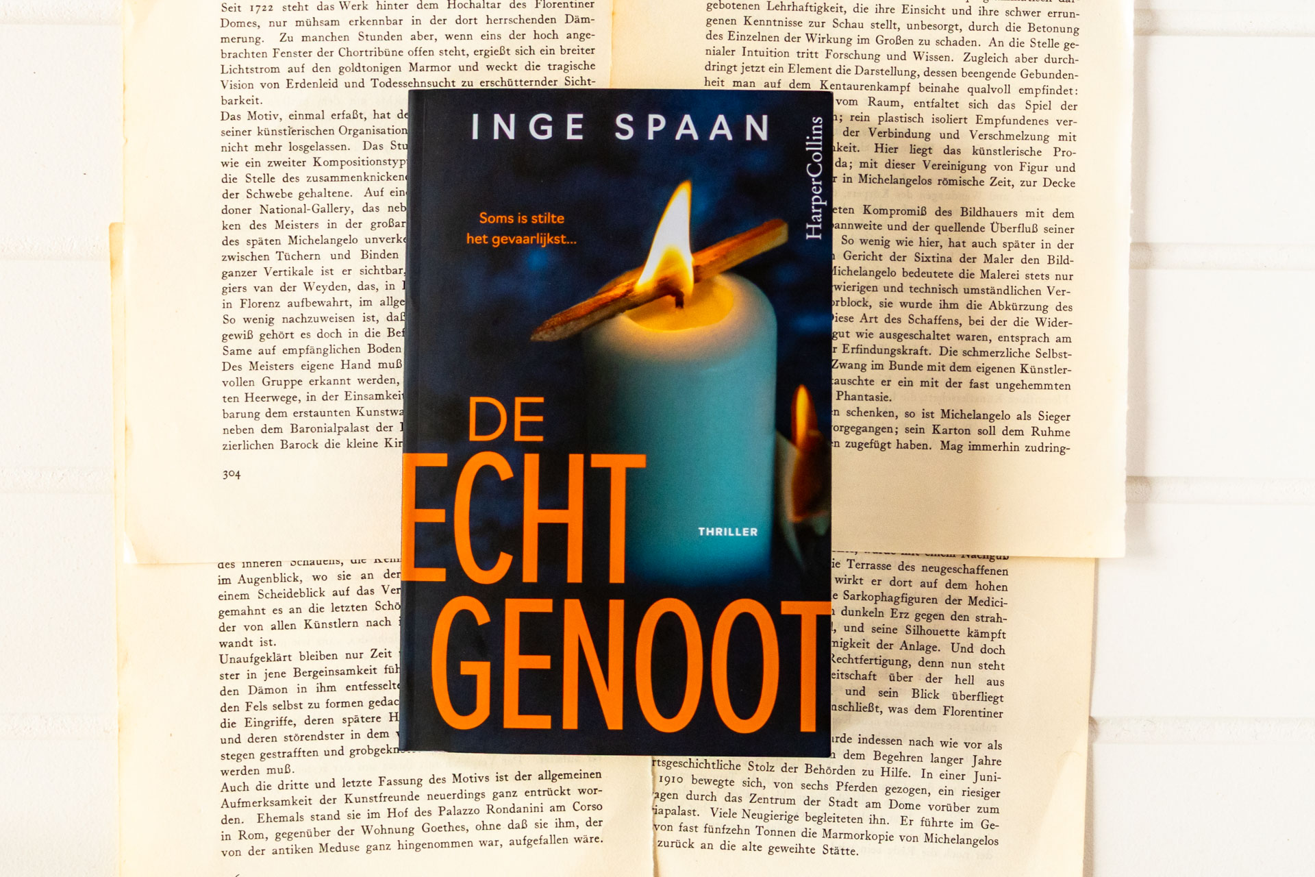 Het thrillerboek De echtgenoot van Inge Spaan ligt op een achtergrond van vergeelde, opengevouwen boekpagina's. De omslag toont een brandende kaars met een lucifer over de vlam, terwijl de titel De echtgenoot, de naam van de auteur en de slogan "Soms is stilte het gevaarlijkst..." goed leesbaar zijn.